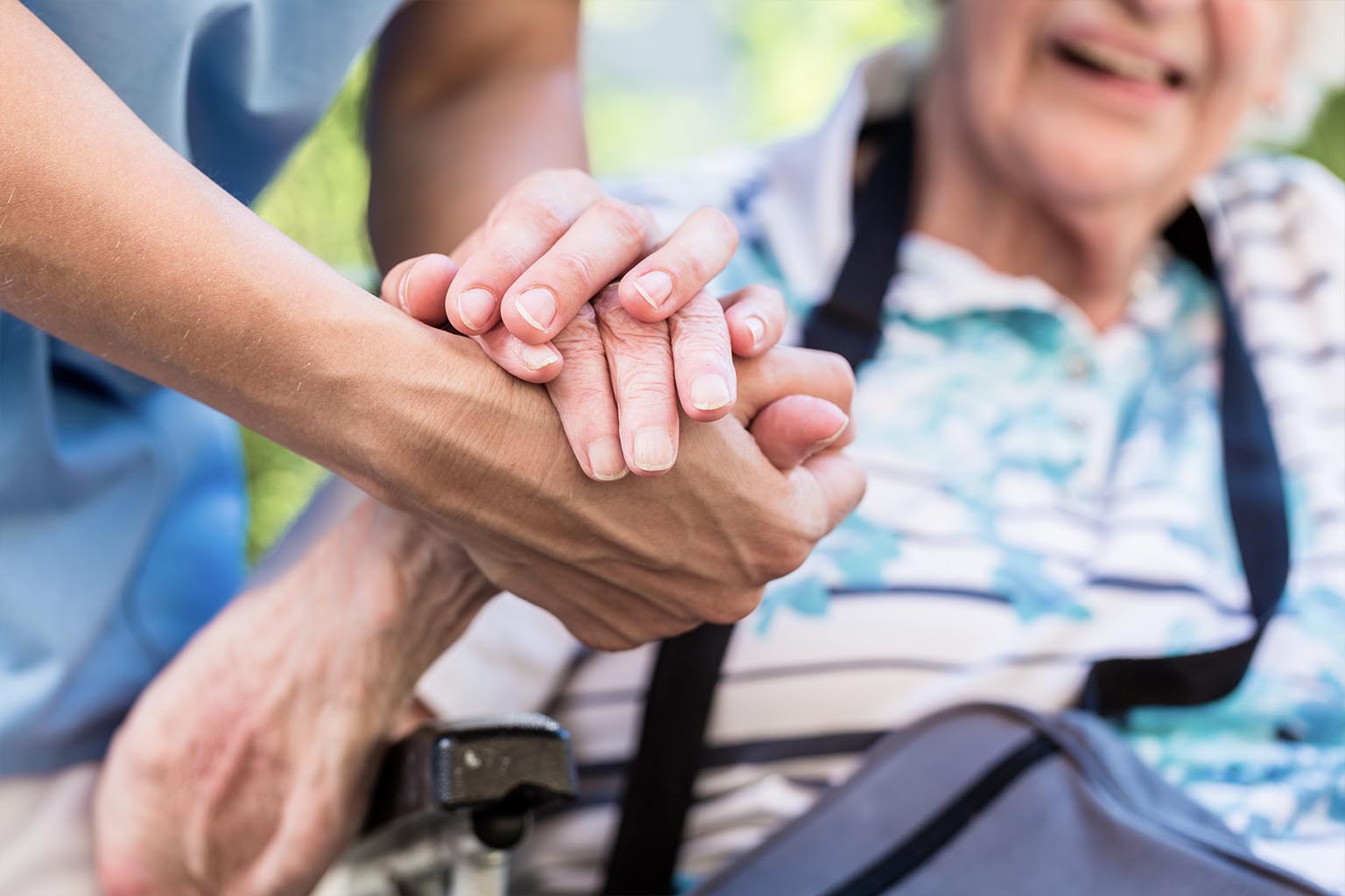 Close up photo of a nurse holding the hand of a senior citizen in a wheel chair.
